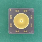 Top view of TI TMX390Z566F ceramic hybrid module with a gold-plated central disc on a green background.